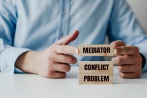 Businessman in a blue shirt arranges wooden blocks with the words Problem, CONFLICT, MEDIATOR.
