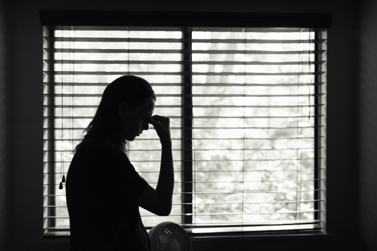 Stressed young woman in a room standing by a window