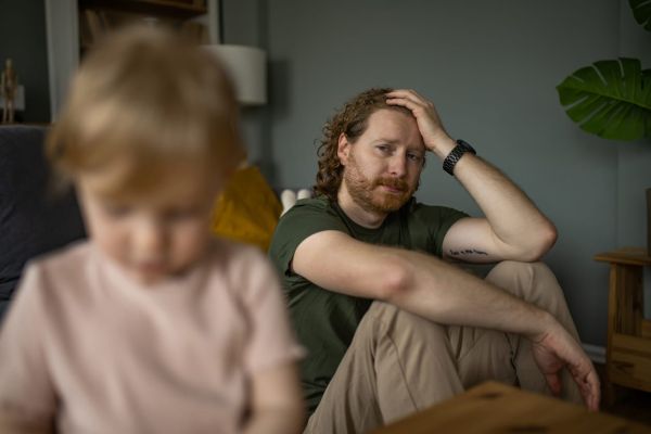 Depressed young father looking at his little daughter is playing at home.