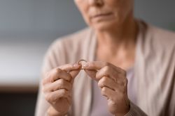 Unhappy unrecognizable senior widow woman holding wedding ring indoors, cropped
